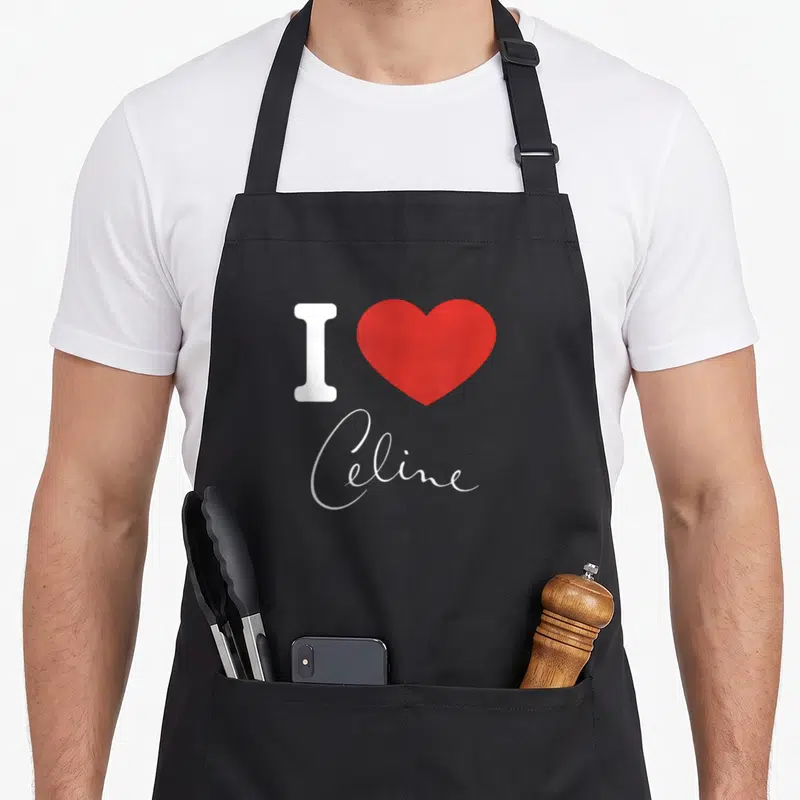 Tablier de cuisine noir avec un grand cœur rouge, la lettre I blanche et le prénom Celine en écriture cursive élégante.