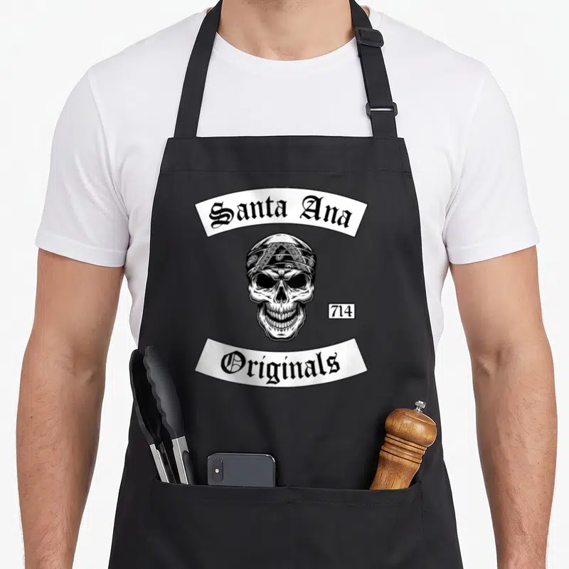 Tablier de cuisine noir avec illustration crâne bandana et texte Santa Ana Originals 714 en typographie gothique blanche.