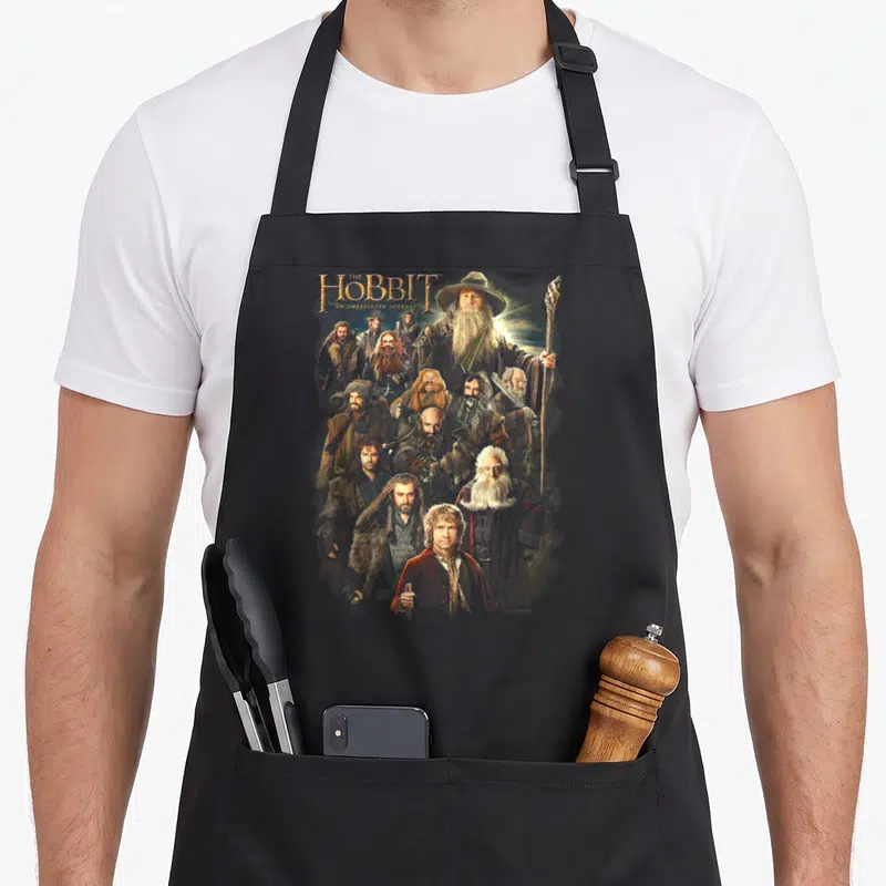 Tablier de cuisine noir avec illustration groupante de personnages de fantasy et texte doré en haut.
