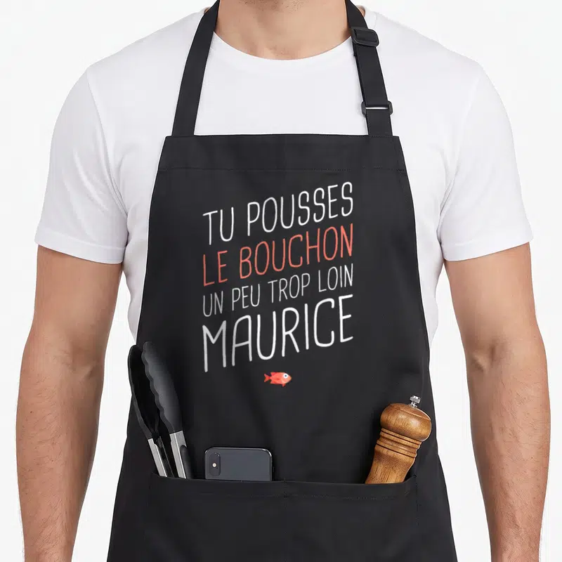 Tablier de cuisine noir avec l'inscription Tu pousses le bouchon un peu trop loin Maurice et un petit poisson rouge en bas.