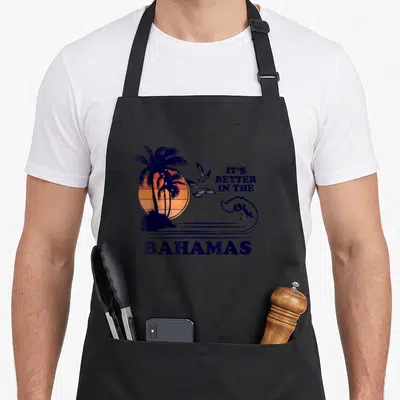 Tablier de cuisine noir avec illustration de palmiers, soleil orange et texte It's Better in the Bahamas en bleu marine.