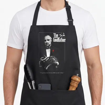 Tablier de cuisine noir avec illustration du parrain tenant un chat et texte The Godfather en haut à droite.