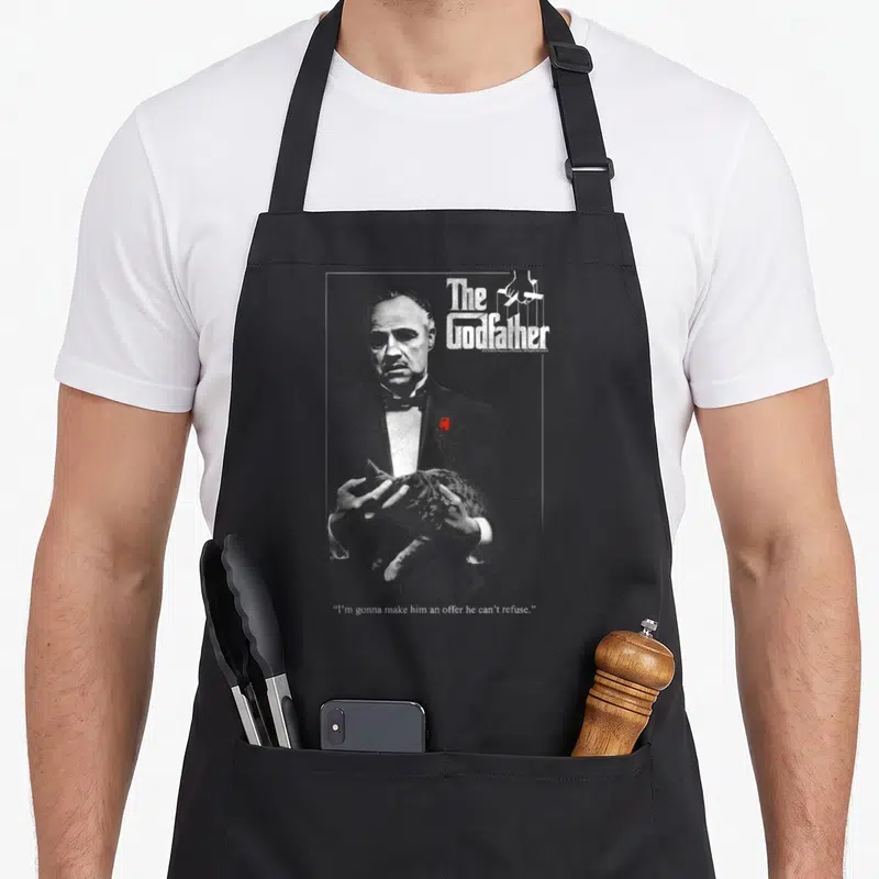 Tablier de cuisine noir avec illustration du parrain tenant un chat et texte The Godfather en haut à droite.