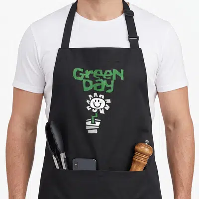 Tablier de cuisine noir avec logo vert Green Day et fleur blanche souriante dans un pot stylisé.