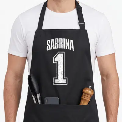 Tablier de cuisine noir avec linscription Sabrina et le chiffre 1 en blanc style maillot de sport vintage.