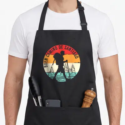 Tablier de cuisine noir avec motif circulaire Buen Camino de Santiago et silhouette de pèlerin.