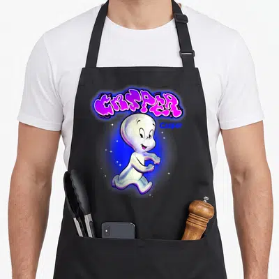 Tablier de cuisine noir avec illustration colorée de Casper le fantôme amical et un logo graffiti rose et bleu.