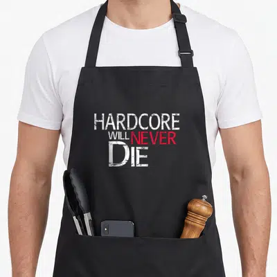 Tablier de cuisine noir avec le texte HARDCORE WILL NEVER DIE en lettres blanches et rouges style usé.