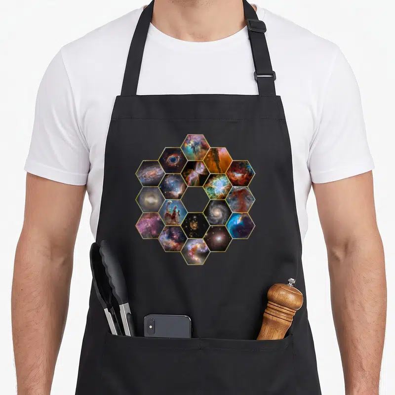 Tablier de cuisine noir avec motif hexagonal regroupant nébuleuses et galaxies spatiales colorées.