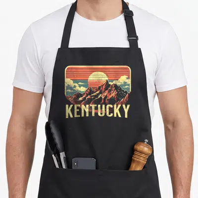 Tablier de cuisine noir avec illustration vintage des montagnes du Kentucky et un soleil couchant orange.