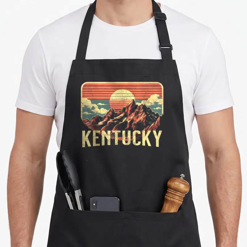 Tablier de cuisine noir avec illustration vintage des montagnes du Kentucky et un soleil couchant orange.