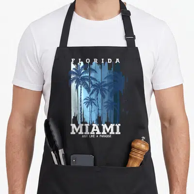 Tablier de cuisine noir avec illustration de palmiers bleus et les mots Florida Miami Just Like A Paradise en blanc.