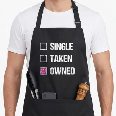 Tablier de cuisine noir avec motif textuel blanc et une case cochée rose contenant un cœur.