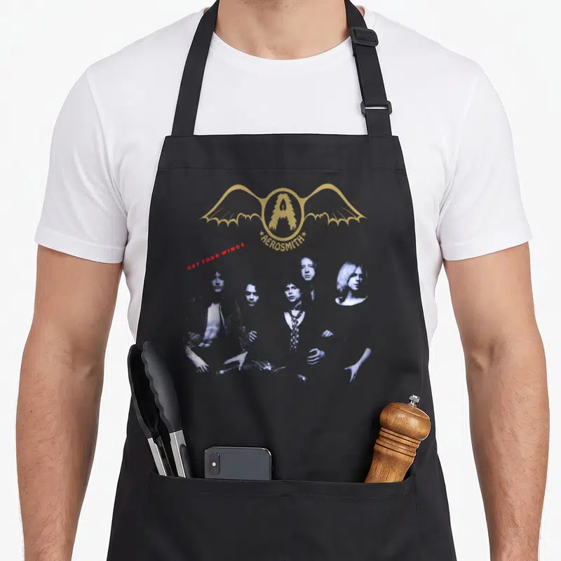 Tablier de cuisine noir avec le logo aux ailes dorées dAerosmith et les portraits bleus des membres du groupe.