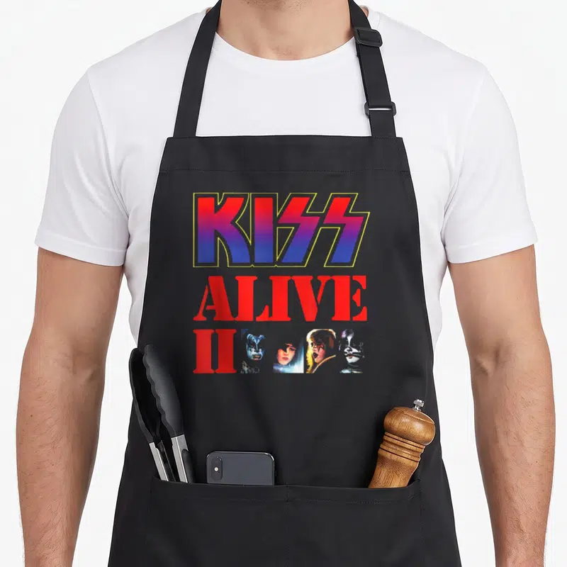 Tablier de cuisine noir avec le logo KISS Alive II et les quatre visages peints du groupe en bas du design.