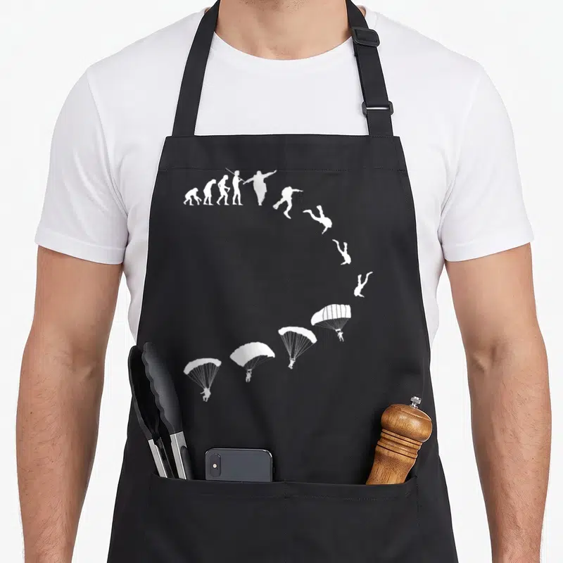 Tablier de cuisine noir avec évolution parachutisme et silhouettes blanches en chute libre puis parachute ouvert.