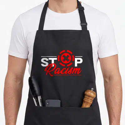 Tablier de cuisine noir avec l'inscription Stop Racism en blanc et rouge et un symbole circulaire stylisé au centre du design.