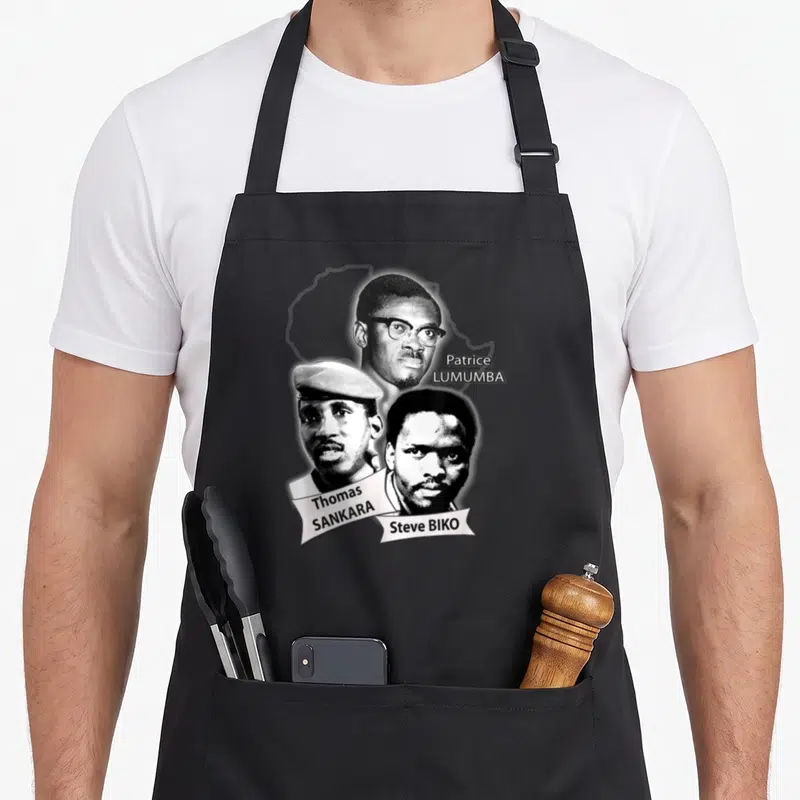 Tablier de cuisine noir avec portraits monochromes de Patrice Lumumba, Thomas Sankara et Steve Biko accompagnés de leurs noms respectifs.