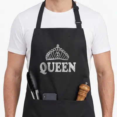 Tablier de cuisine noir avec une couronne de reine scintillante et le mot QUEEN en lettres pailletées argentées.