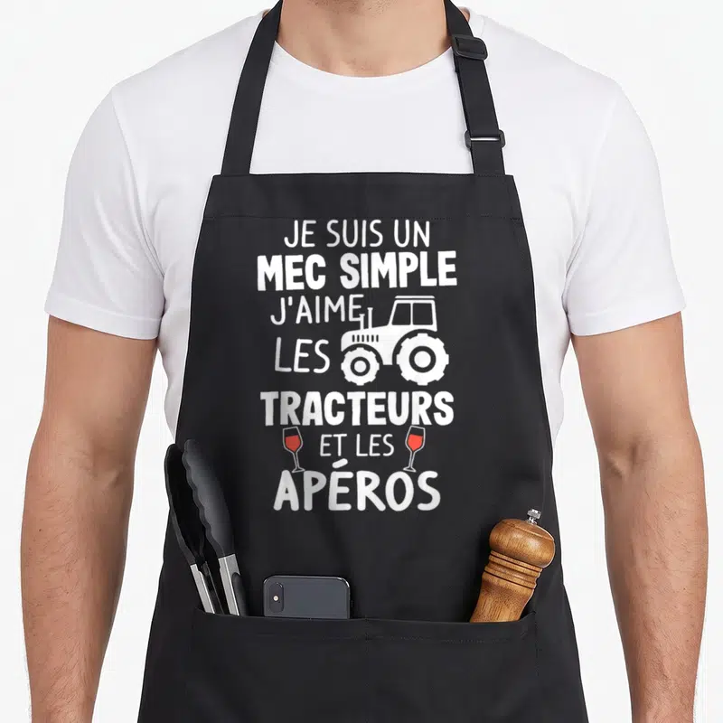 Tablier de cuisine noir avec inscription blanche Je suis un mec simple j'aime les tracteurs et les apéros illustrée d'un engin et deux verres de vin rouge.