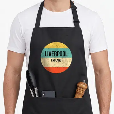 Tablier de cuisine noir avec un motif circulaire coloré affichant les mots Liverpool England en typographie noire.