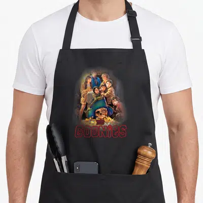 Tablier de cuisine noir avec illustration des personnages du film The Goonies et un crâne de pirate au milieu de trésors.