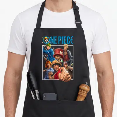 Tablier de cuisine noir avec une illustration colorée du logo One Piece et six personnages animés posant ensemble.
