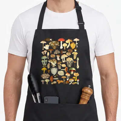 Tablier de cuisine noir avec une illustration de champignons fourragers colorés et variés sur fond uni.