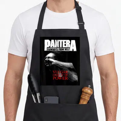 Tablier de cuisine noir avec le logo Pantera, l'inscription Cowboys From Hell et une illustration monochrome avec le titre Vulgar Display of Power en rouge.