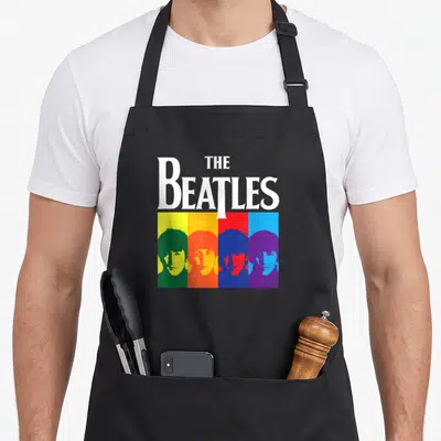 Tablier de cuisine noir avec logo The Beatles et portraits colorés style pop art sur bandes verticales.