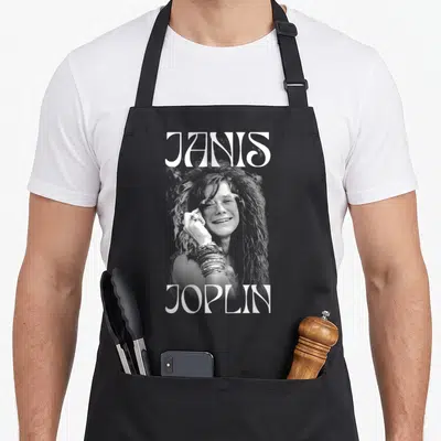 Tablier de cuisine noir avec portrait blanc de Janis Joplin et son nom en grandes lettres stylisées sur le devant.