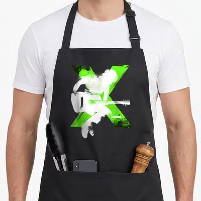 Tablier de cuisine noir avec grand X vert et silhouettes blanches d'Ed Sheeran jouant de la guitare.