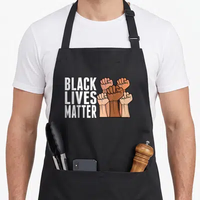 Tablier de cuisine noir avec inscription Black Lives Matter et illustration de cinq poings levés de couleurs différentes.
