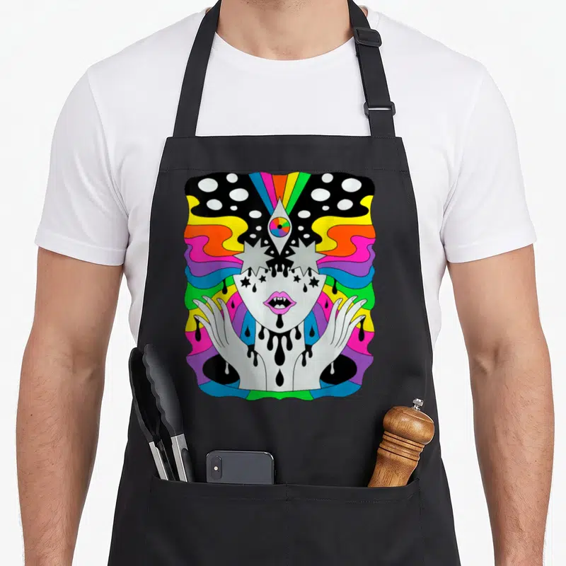 Tablier de cuisine noir avec illustration colorée d'une figure psychédélique au troisième œil et rayons arc-en-ciel.