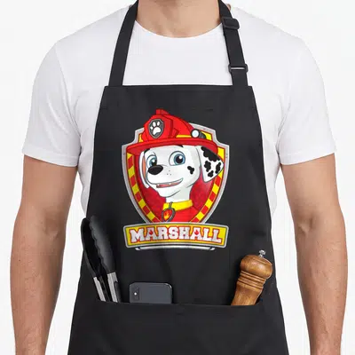 Tablier de cuisine noir avec l'illustration du chien pompier Marshall dans un insigne rouge et jaune portant son nom.