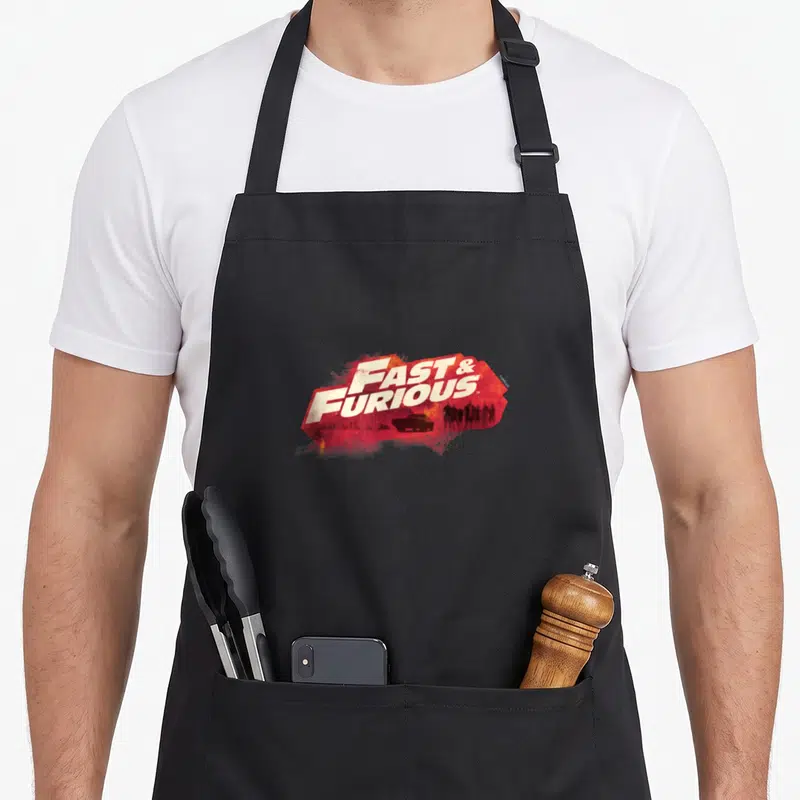 Tablier de cuisine noir avec le logo Fast & Furious en rouge vif et silhouettes sombres au centre.