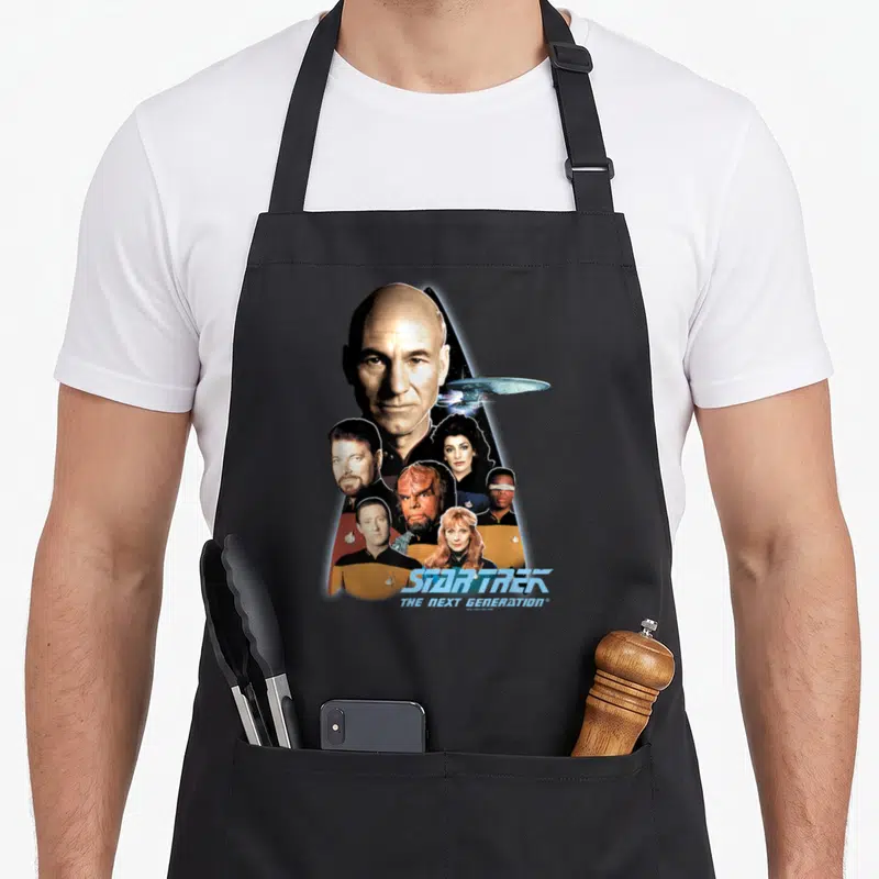 Tablier de cuisine noir avec le capitaine Picard et l'équipage du Starship Enterprise dans un logo Delta stylisé.