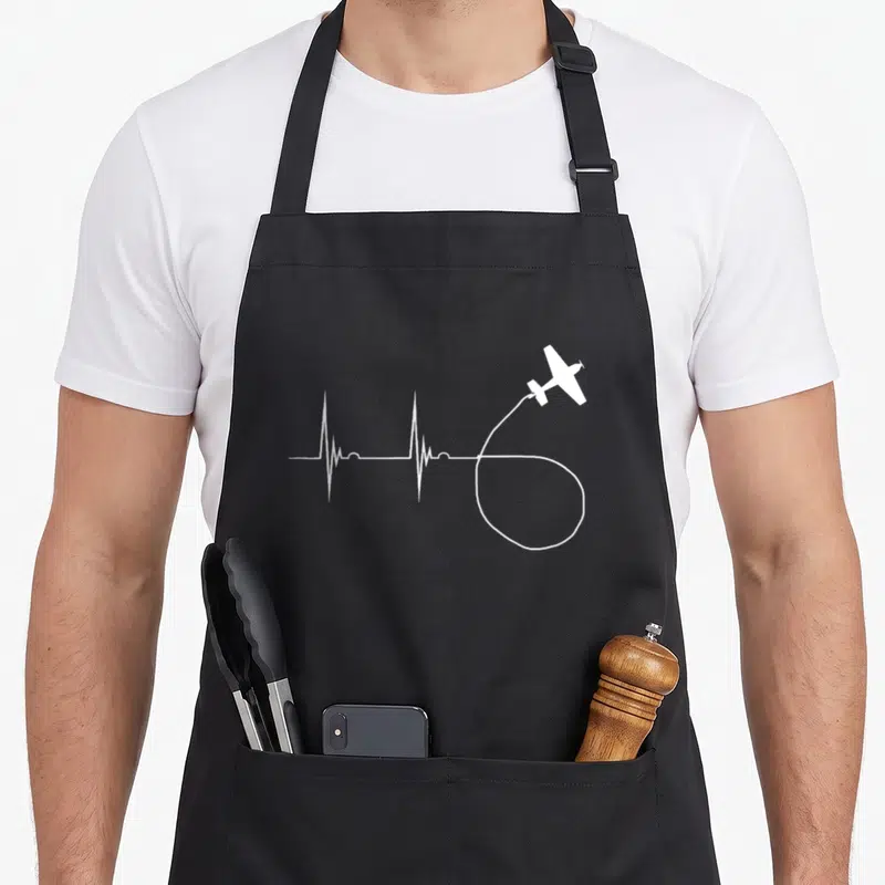Tablier de cuisine noir avec tracé blanc ECG formant une boucle tirée par un petit avion type Glider
