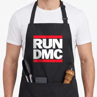 Tablier de cuisine noir avec logo RUN DMC en lettres blanches encadrées par des bandes rouges horizontales.