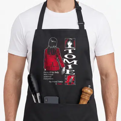 Tablier de cuisine noir avec silhouette rouge dos tourné, texte blanc vertical Tomie et vignettes d'illustrations macabres en haut et bas à droite.