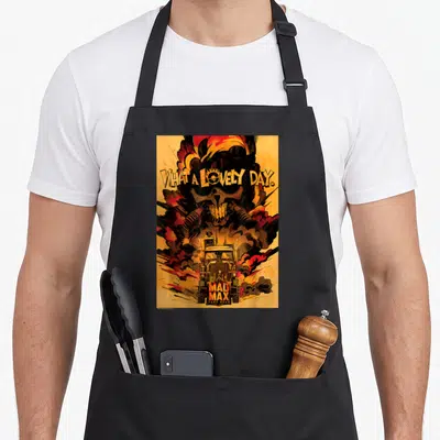 Tablier de cuisine noir avec illustration Mad Max et texte « What A Lovely Day » sur fond orange.