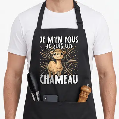 Tablier de cuisine noir avec un chameau cartoon beige et le texte Je m'en fous je suis un chameau en blanc.