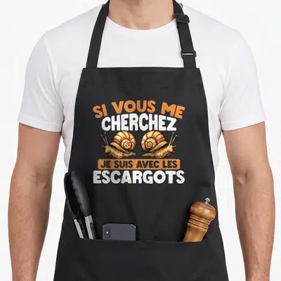 Tablier de cuisine noir avec deux escargots dessinés et le texte Si Vous Me Cherchez Je Suis Avec Les Escargots en orange et blanc.