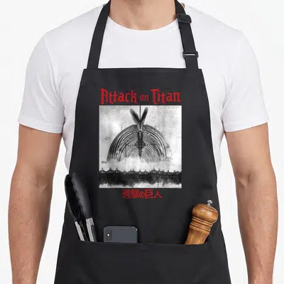 Tablier de cuisine noir avec illustration Attack on Titan The Rumbling en noir et blanc et texte rouge.