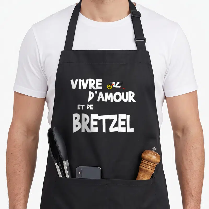 Tablier de cuisine noir avec texte blanc Vivre d'amour et de Bretzel et illustration de cèdre portant un bretzel.
