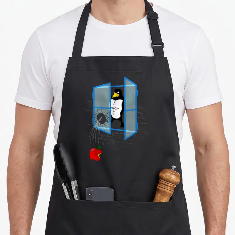 Tablier de cuisine noir avec un pingouin musclé brisant une fenêtre bleue et une pomme rouge mordue tombant en dessous.