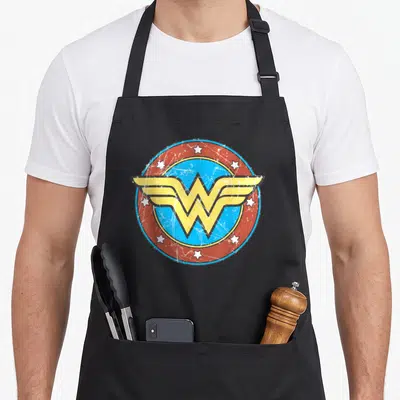 Tablier de cuisine noir avec le logo Wonder Woman en cercle rouge et bleu, style vintage égréné et étoiles blanches.