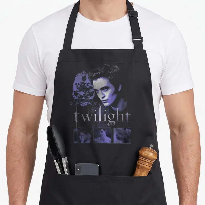 Tablier de cuisine noir avec motif violet et argenté représentant un portrait de vampire, des armoiries stylisées et trois vignettes carrées en bas.