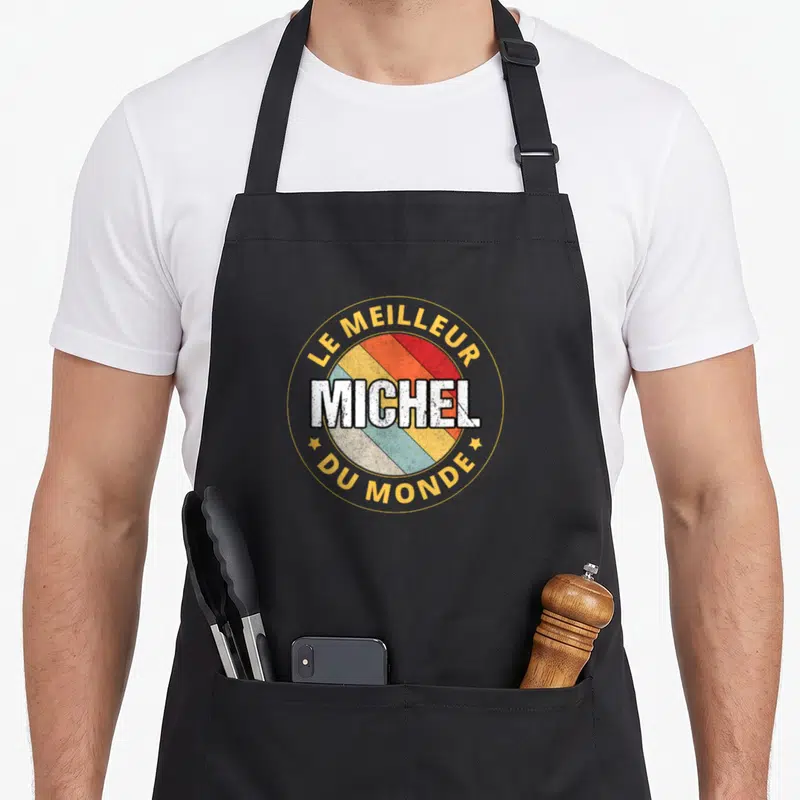 Tablier de cuisine noir avec logo circulaire coloré affichant le prénom Michel et l'inscription le meilleur du monde.