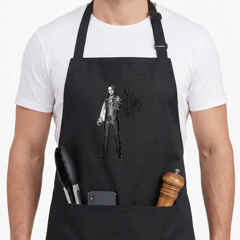 Tablier de cuisine noir avec une illustration monochrome d'un personnage aux cheveux longs et le texte All magic comes with a price.